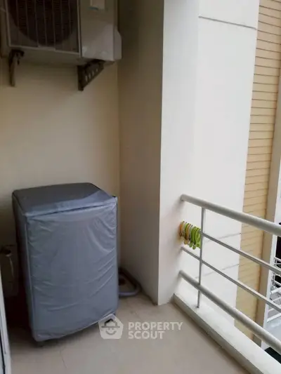 Compact balcony with washing machine and railing, ideal for urban living.