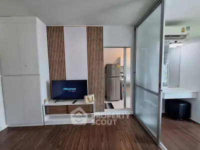 Modern living room with sleek TV unit and view into contemporary kitchen with stainless steel fridge.