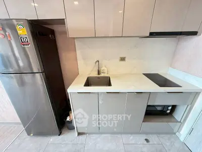 Modern compact kitchen with sleek cabinetry and built-in appliances, featuring a stainless steel fridge and electric cooktop.