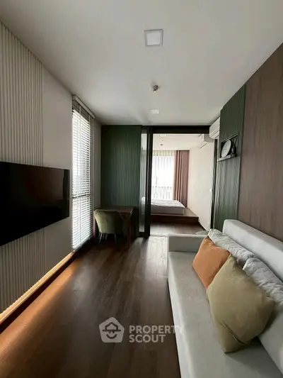 Modern living room with sleek design and natural light leading to a cozy bedroom.