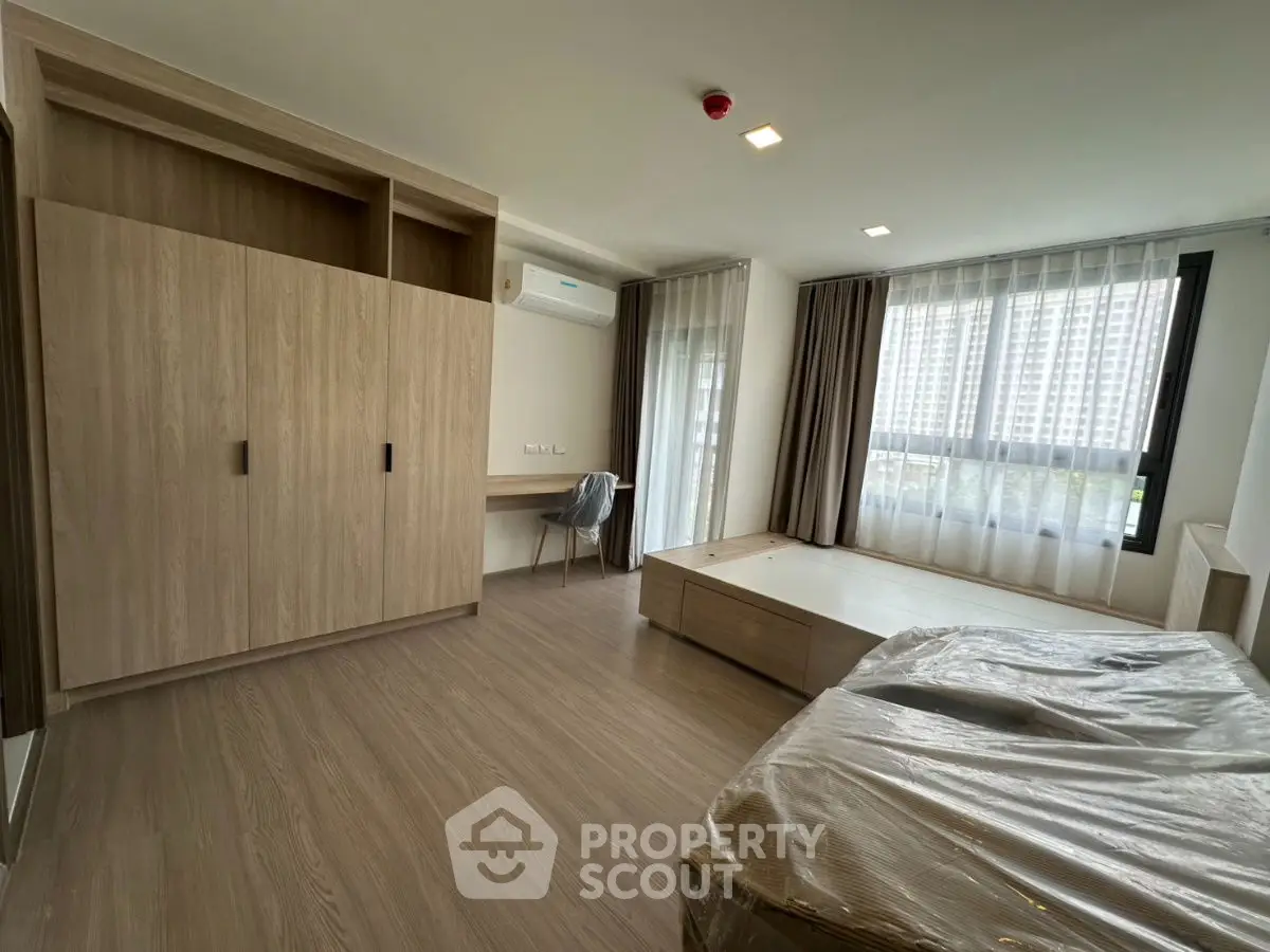 Spacious modern bedroom with large windows and wooden flooring in a high-rise apartment.