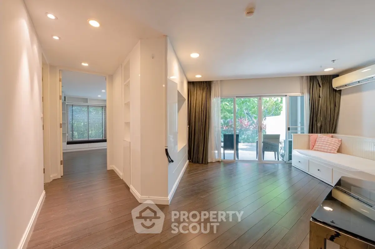 Spacious modern living room with large windows and garden view, featuring sleek hardwood floors and elegant decor.