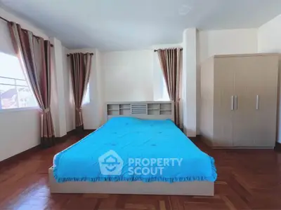 Spacious bedroom with large windows and wooden flooring, featuring a cozy bed and ample storage.