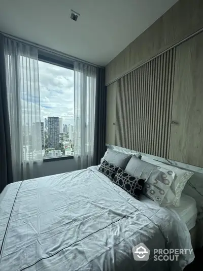 Modern bedroom with large window offering stunning city view in high-rise apartment.