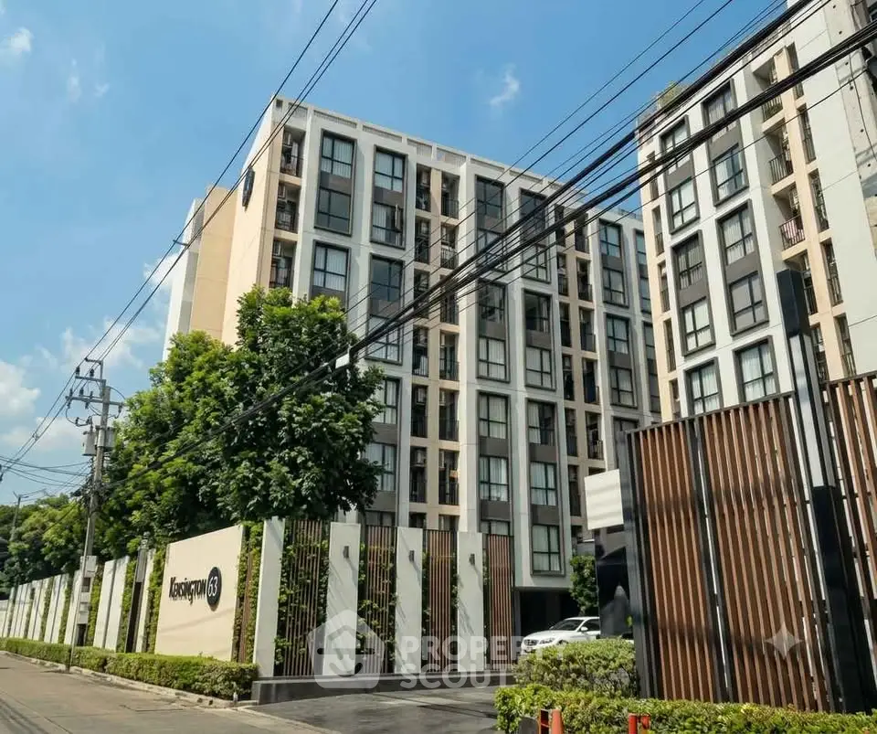 Modern apartment building exterior with lush greenery and clear blue sky.