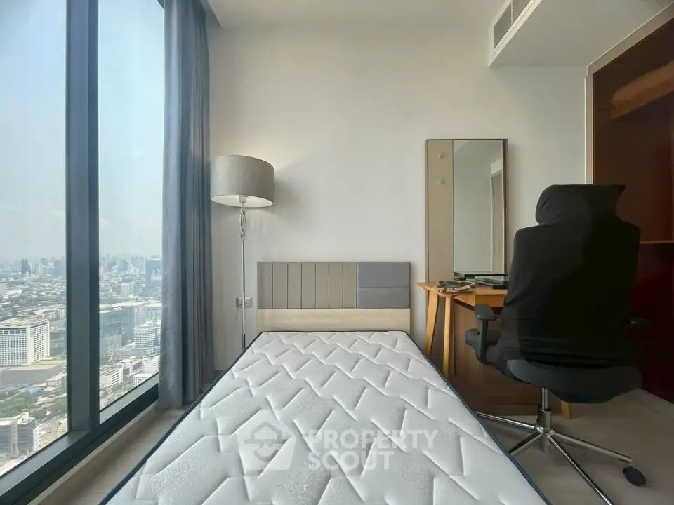 Modern bedroom with city view, featuring a sleek desk and comfortable chair, perfect for urban living.
