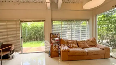Spacious living room with large windows and garden view, featuring cozy leather sofa and natural light.