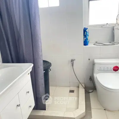 Modern bathroom with white tiles and sleek fixtures, featuring a shower area and toilet.