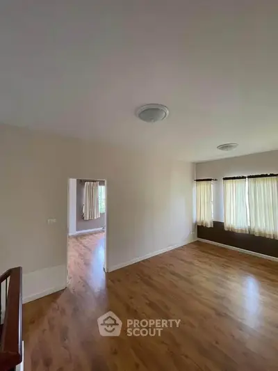 Spacious empty room with wooden flooring and large windows, perfect for customization.