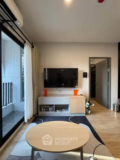 Modern living room with large TV, stylish furniture, and natural light from balcony window.