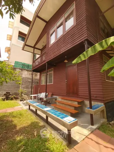 Charming two-story wooden house with a cozy porch and lush garden, perfect for serene living.