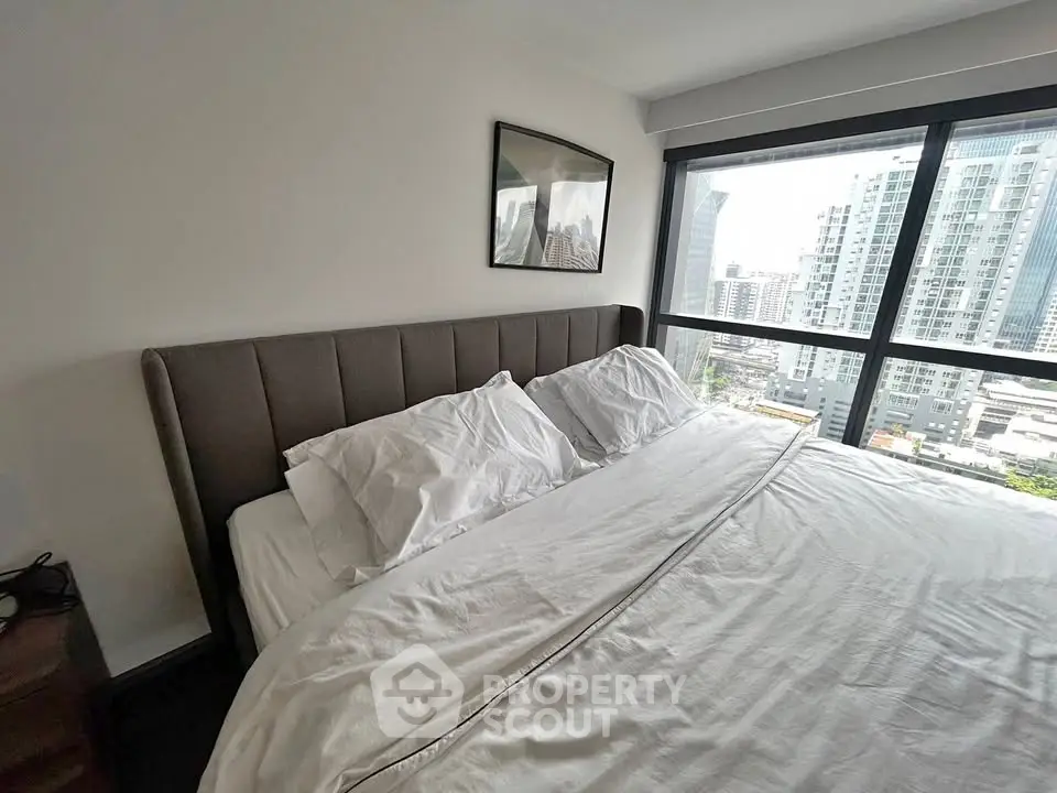 Modern bedroom with large window offering stunning city views in a high-rise apartment.