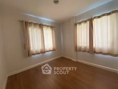 Spacious empty room with wooden flooring and large windows, perfect for customization.