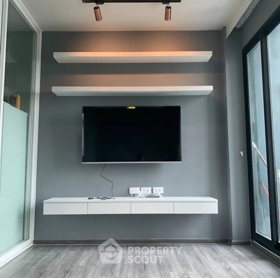 Modern living room with sleek TV setup and floating shelves, featuring stylish flooring and large windows.