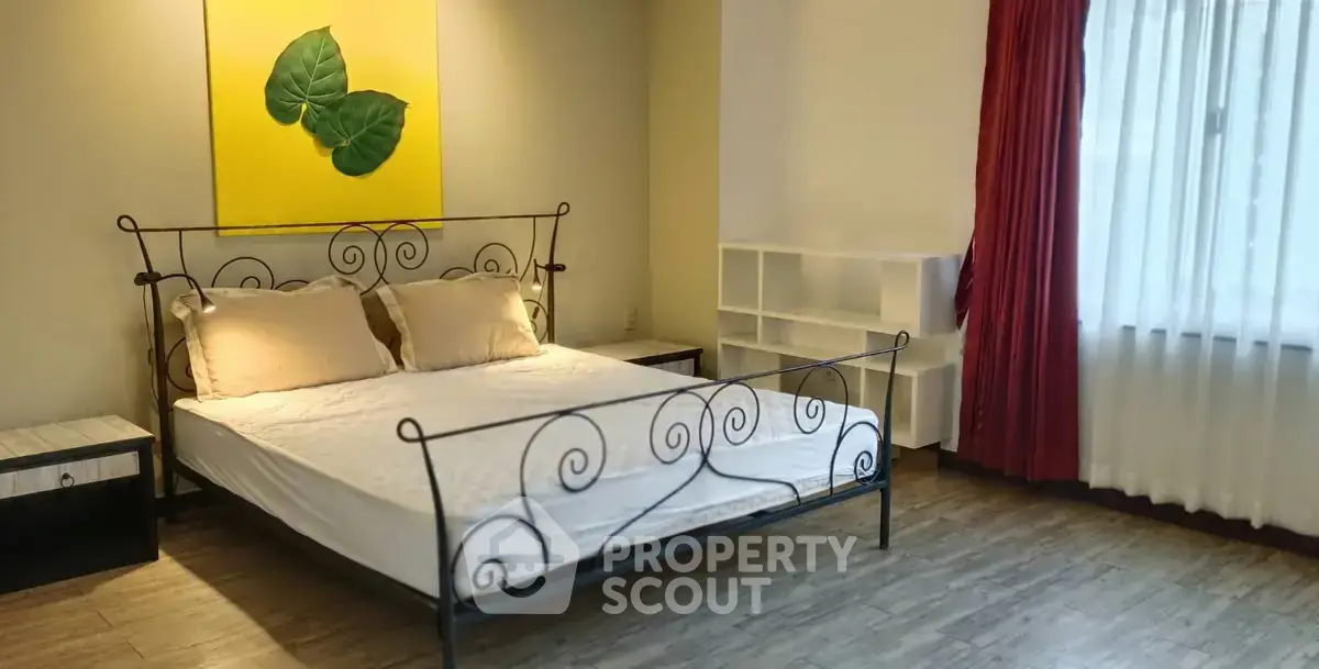 Spacious bedroom with elegant metal bed frame and large window with red curtains.