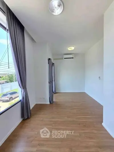 Spacious empty room with wooden flooring and large windows, perfect for customization.