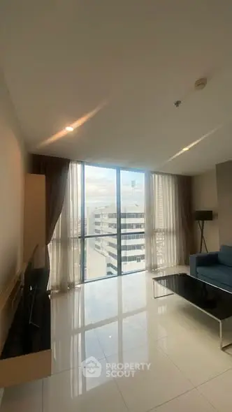 Modern living room with large windows and city view, featuring sleek furniture and glossy flooring.