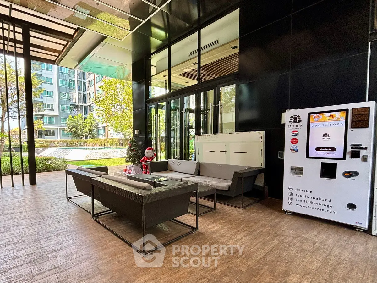 Modern condo entrance with seating area and vending machine, lush garden view.