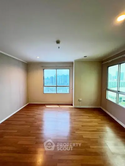Spacious empty living room with large windows and wooden flooring, offering a bright and airy atmosphere.