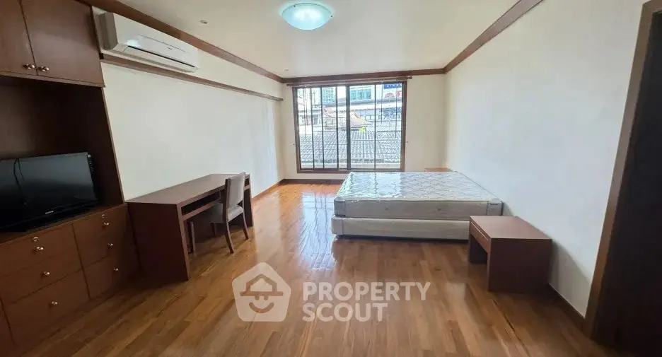 Spacious bedroom with wooden flooring and natural light, featuring a bed, desk, and TV unit.