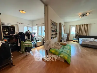 Spacious bedroom with wooden flooring and ample natural light, featuring a cozy bed and organized storage.