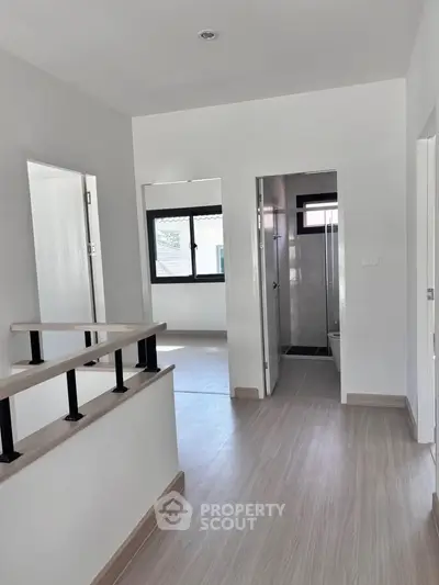 Modern hallway with light wood flooring and white walls leading to a bright room.