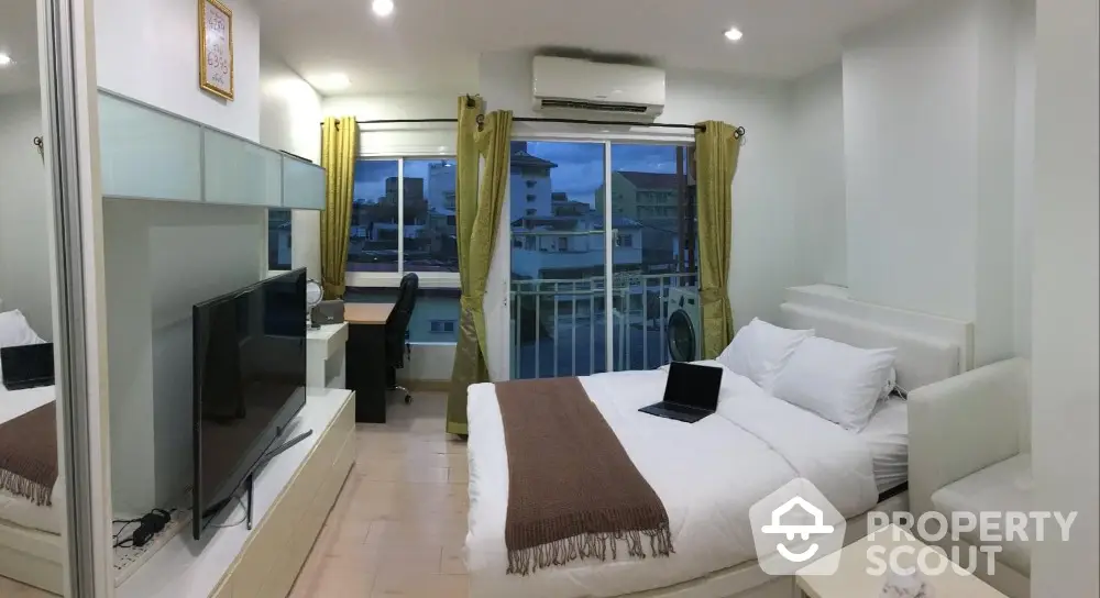 Modern bedroom with city view, featuring a cozy bed, large TV, and workspace.