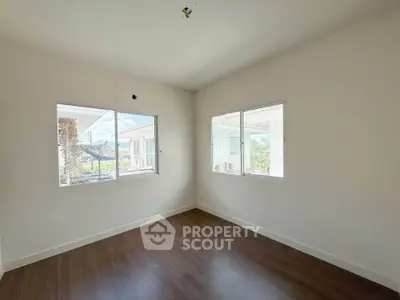 Bright empty room with wooden flooring and large windows in modern home.