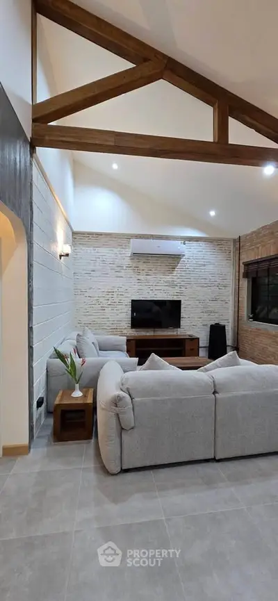 Spacious living room with modern decor and exposed wooden beams, featuring a cozy seating area and entertainment setup.