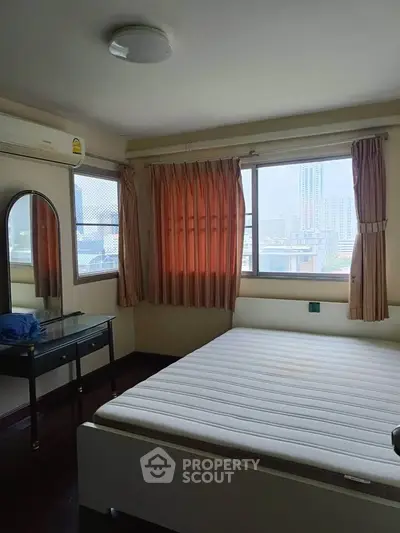 Cozy bedroom with large windows offering city views, featuring a comfortable bed and elegant dressing table.