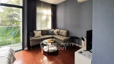 Modern living room with sleek furniture and large window offering lush garden view.