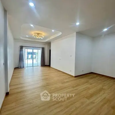 Spacious empty living room with wooden flooring and elegant ceiling lights.