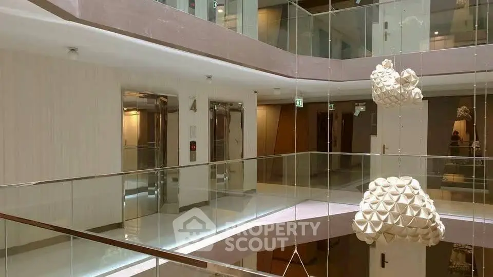 Modern building interior with glass railings and artistic sculptures near elevators.