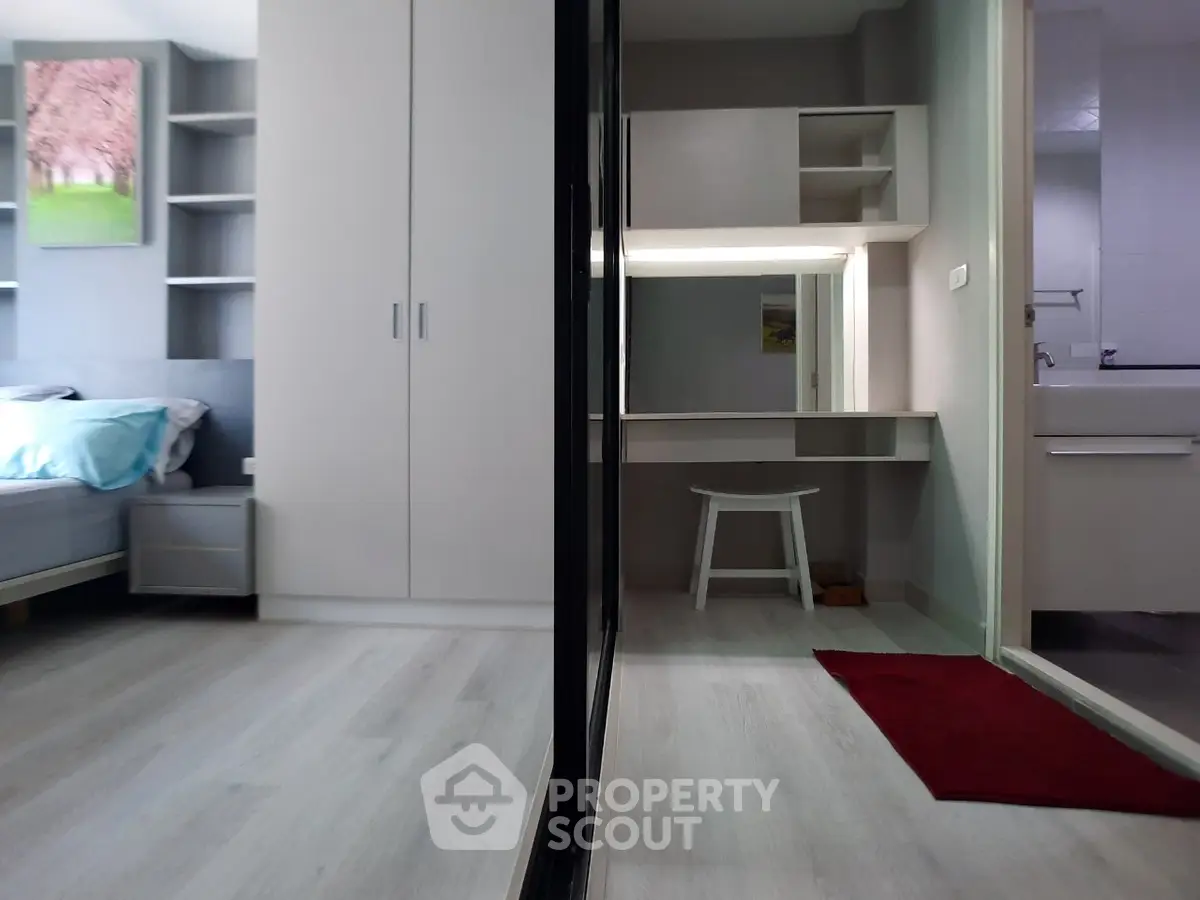 Modern bedroom with sleek wardrobe and vanity, featuring light wood flooring and minimalist decor.