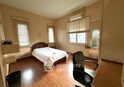 Spacious bedroom with wooden flooring and natural light, featuring a cozy bed and work desk.