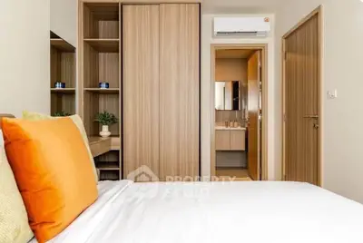 Modern bedroom with wooden furniture and ensuite bathroom, featuring a cozy bed with vibrant pillows.