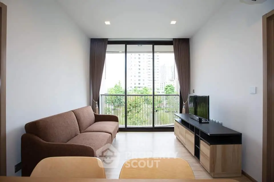 Modern living room with large window and city view, featuring a brown sofa and sleek entertainment unit.