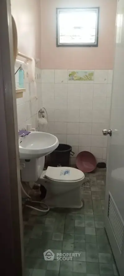 Compact bathroom with tiled walls and floor, featuring a sink and toilet under a small window.