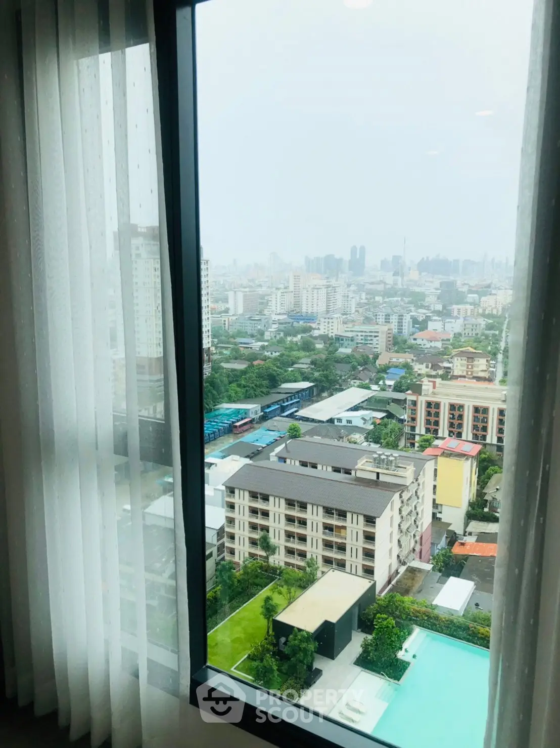 Stunning cityscape view from high-rise apartment window overlooking pool and urban skyline.