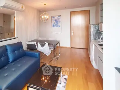 Modern living room with blue sofa, dining area, and sleek kitchen in open layout apartment.