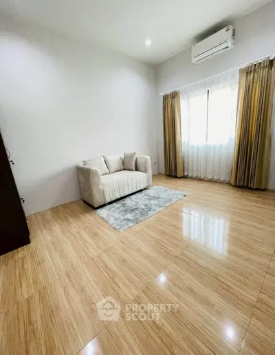 Spacious living room with elegant flooring and cozy sofa, featuring natural light from large window.
