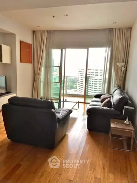 Spacious living room with leather sofas and a city view balcony.