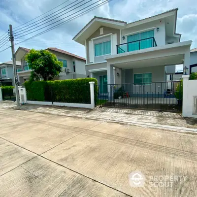 Modern two-story house with balcony and lush greenery in a serene neighborhood.