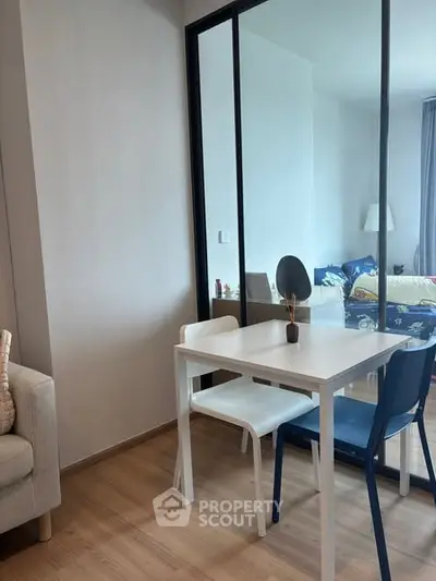 Modern dining area with sleek white table and chairs, adjacent to a cozy living space.