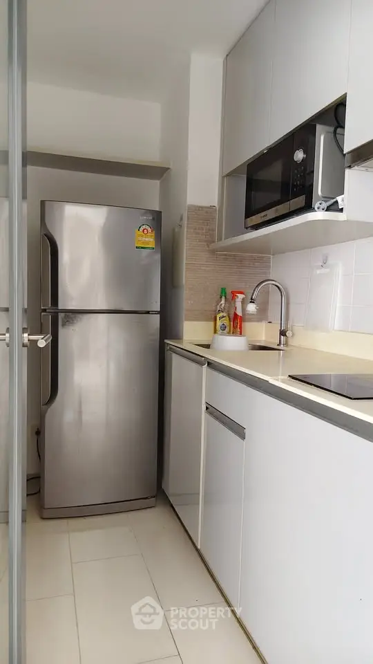 Modern kitchen with stainless steel fridge and microwave, sleek cabinetry, and bright lighting.