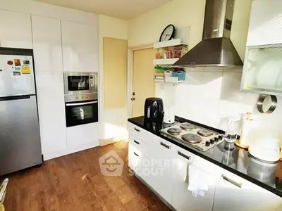 Modern kitchen with sleek appliances and wooden flooring, featuring a stainless steel fridge and oven.