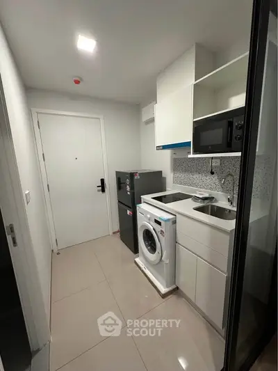 Modern compact kitchen with washing machine and microwave in sleek apartment.