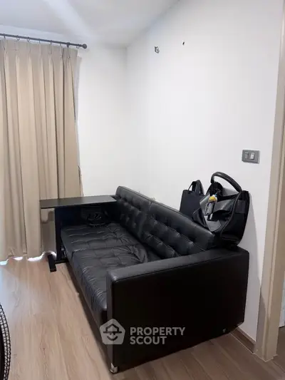 Modern living room with sleek black leather sofa and wooden flooring, perfect for stylish urban living.