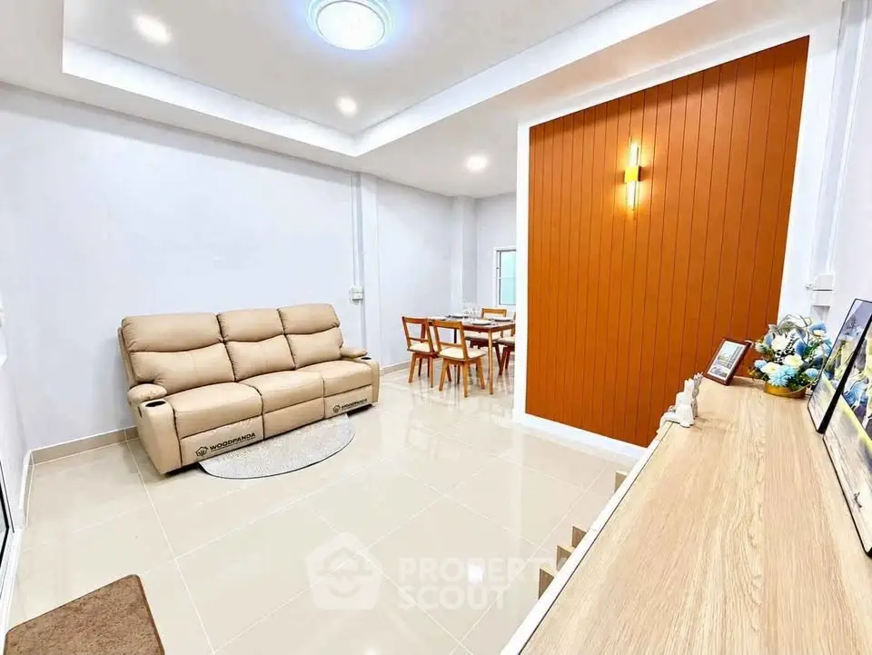 Modern living room with beige sofa and dining area, featuring sleek design and warm lighting.