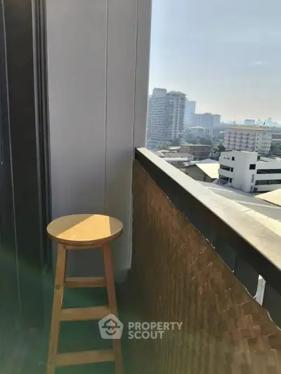 Charming balcony with city view and wooden stool, perfect for relaxation.